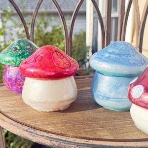 May include: A collection of decorative mushroom-shaped objects in various colors, including red, green, and blue, with white bases. The mushrooms are arranged on a wooden surface, suggesting a whimsical or fantasy theme.