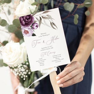 May include: Wedding ceremony program fan with a floral design featuring purple and pink flowers. The program lists the order of events for the wedding ceremony of Tom and Helen, taking place on September 26, 2019 at St. Mary's Church in Minnesota.