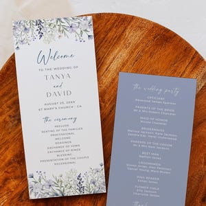 Op de afbeelding: Twee huwelijksprogramma's op een houten oppervlak. Het linkerprogramma is wit met blauwe bloemaccenten en de tekst "Welkom bij de bruiloft van Tanya en David". Het rechterprogramma is blauw met details van de bruiloft.