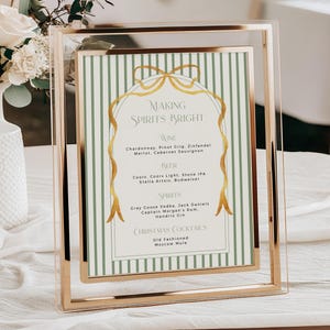 May include: A framed sign with the text "MAKING SPIRITS BRIGHT" in gold lettering. The sign lists wine, beer, spirits, and Christmas cocktails. The frame is gold and the background is green and white striped.