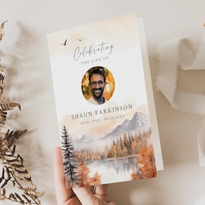 Könnte beinhalten: Eine Gedenkkarte mit einer Aquarell-Illustration eines Bergsees und eines Waldes. Die Karte zeigt ein Foto eines lächelnden Mannes und den Text "Celebrating the life of Shaun Parkinson 09.01.19XX - 08.22.20XX".