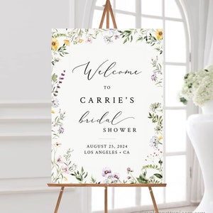 May include: A white bridal shower welcome sign with a floral border. The sign says "Welcome to Carrie's bridal shower, August 25, 2024, Los Angeles, CA".