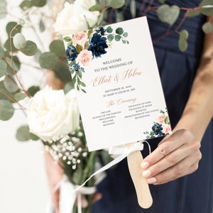 May include: A wedding ceremony program fan with a floral design featuring navy blue and pink flowers. The program lists the order of the ceremony, including the prelude, seating of the families, processional, welcome readings, exchange of vows, exchange of rings, blessing, presentation of the couple, and recessional. The text reads "Welcome to the wedding of Elliot & Helen, September 26, 2020, St. Mary's Church, MN."