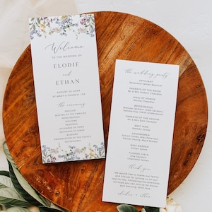 May include: Wedding ceremony programme cards featuring floral designs. The cards display the names Elodie and Ethan, the date August 25, 20XX, and the venue St. Mary's Church, CA. The ceremony details are outlined on the left card, while the wedding party is listed on the right card.