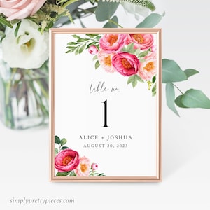 May include: A white table number card with pink floral illustrations. The card has the text "table no. 1" and "Alice + Joshua August 20, 2023".