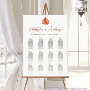 May include: A wedding seating plan displayed on an easel. The sign displays the names "Matilda + Andrew" and the date "October 25th, 2022". Guest names are listed under table numbers. An orange leaf decorates the top of the sign.