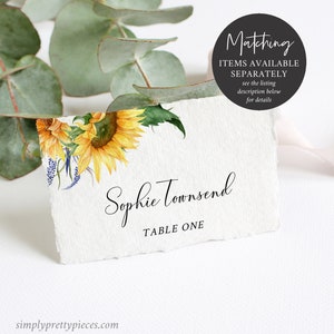 K&ouml;nnte beinhalten: Eine wei&szlig;e Tischkarte mit einem Aquarell-Sonnenblumen-Design. Der Text "Sophie Townsend" und "Tisch Eins" ist auf die Karte gedruckt.