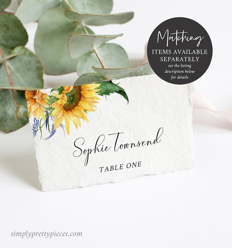 K&ouml;nnte beinhalten: Eine wei&szlig;e Tischkarte mit einem Aquarell-Sonnenblumen-Design. Der Text "Sophie Townsend" und "Tisch Eins" ist auf die Karte gedruckt.