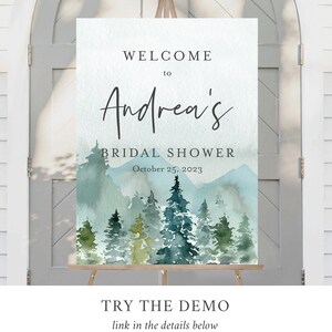 Op de afbeelding: Een aquarel-illustratie van een boslandschap met bergen op de achtergrond. De tekst "WELCOME to Andrea's BRIDAL SHOWER October 25, 2023" staat op het bord gedrukt.