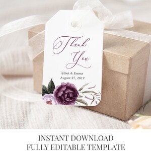 May include: A white wedding favor tag with a purple floral design and the text "Thank You" in a cursive font. The tag also includes the names "Elliot & Emma" and the date "August 27, 2019".