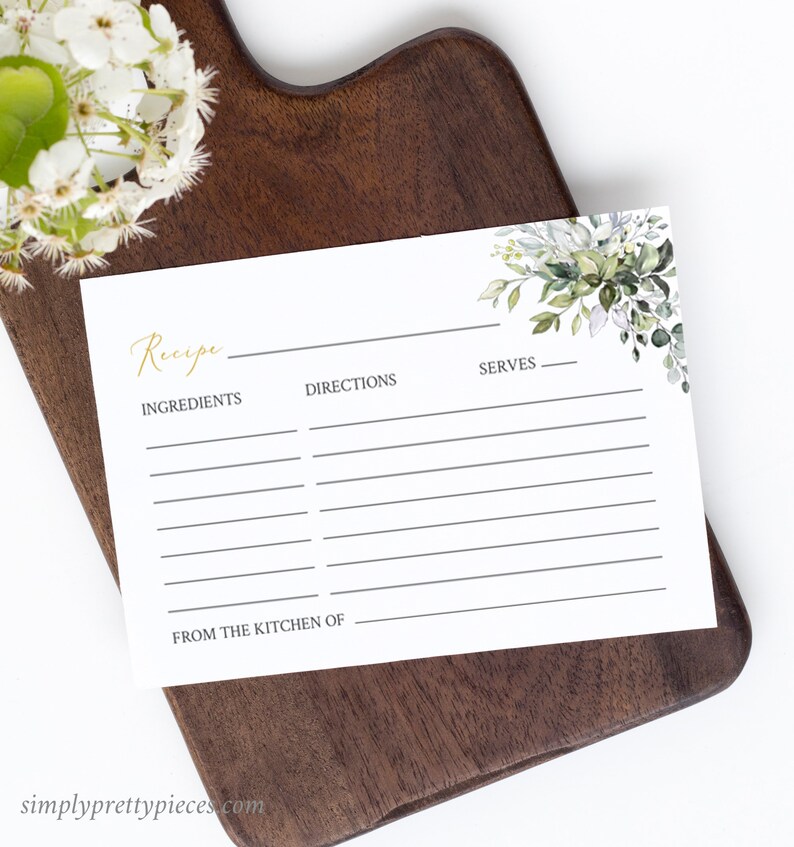 May include: A white recipe card with gold script that reads "Recipe", "Ingredients", "Directions", and "Serves". The card has a floral design in the upper right corner and is on a dark wooden cutting board. The text "FROM THE KITCHEN OF" is at the bottom.