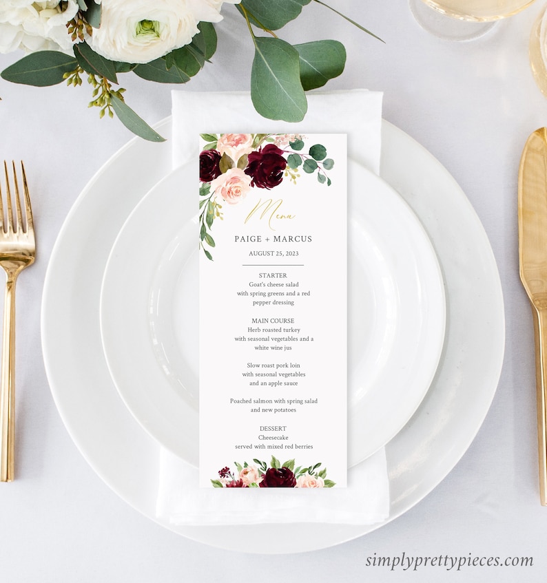 May include: A wedding menu card with floral accents in burgundy, blush, and green, featuring the names "Paige + Marcus" and the date "August 25, 2023." The menu includes starter, main course, and dessert options. The card is set on a white plate with gold cutlery.