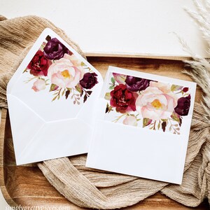 Puede incluir: Dos sobres blancos con un diseño floral en la solapa. El diseño presenta flores de color burdeos, rosa y blanco con hojas verdes.