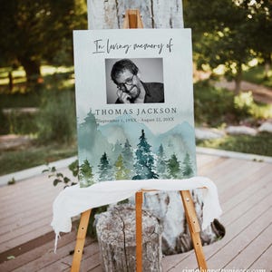 May include: A memorial sign with a watercolor background of a forest scene. The sign reads "In loving memory of Thomas Jackson, September 1, 19XX - August 22, 20XX". A black and white photo of Thomas Jackson is in the upper right corner of the sign.