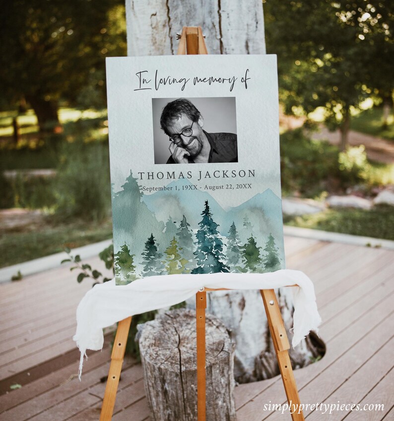 May include: A memorial sign with a watercolor background of a forest scene. The sign reads "In loving memory of Thomas Jackson, September 1, 19XX - August 22, 20XX". A black and white photo of Thomas Jackson is in the upper right corner of the sign.