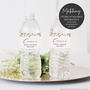 May include: Two clear plastic water bottles with labels that say "Carrie's Bridal Shower August 25, 2024". The labels have a floral design with yellow, purple, and green flowers.