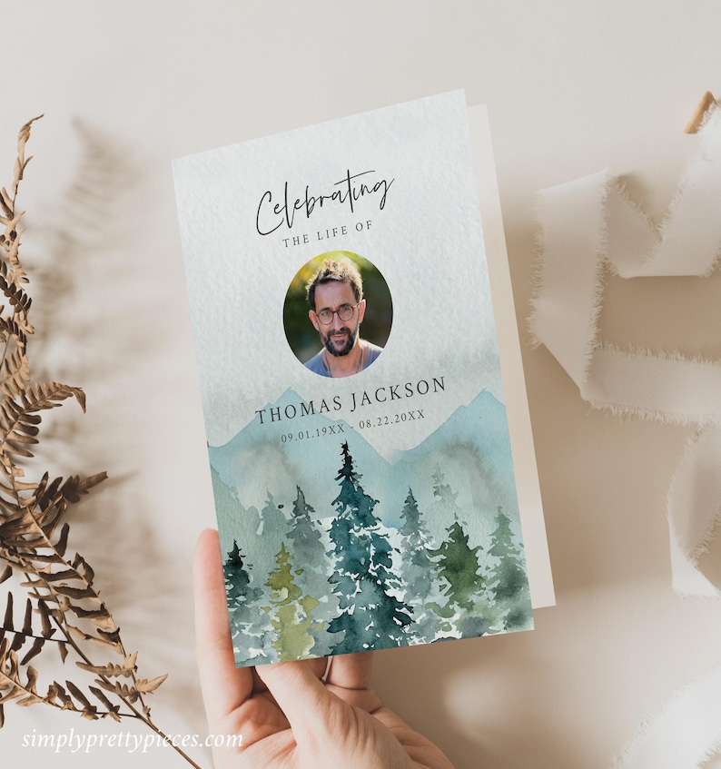 May include: A watercolor memorial card with a photo of a man in a circle. The card has a blue and green watercolor background with mountains and trees. The text reads "Celebrating the Life of Thomas Jackson 09.01.19XX - 08.22.20XX".