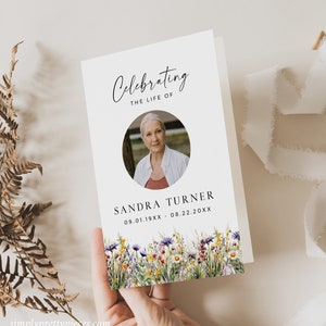 Op de afbeelding: Een witte rouwkaart met een foto van een vrouw en de tekst "Celebrating the life of Sandra Turner 09.01.19XX - 08.22.20XX". De kaart is versierd met een rand van kleurrijke wilde bloemen.