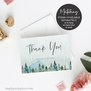 May include: Thank You card with a watercolor illustration of a mountain range and pine trees in shades of blue and green. The text "Thank You" is written in a handwritten font. The names "Helen & Elliot" are printed below the illustration.