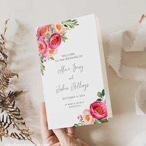 Op de afbeelding: Huwelijksvoltrekkingsprogramma met een roze en witte bloemenrand. De tekst luidt "Welkom op de bruiloft van Alice Young en Joshua Hollings, 26 september 20XX, St. Mary's Church, Minnesota."
