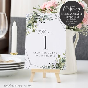 Puede incluir: Tarjeta de mesa de boda n&uacute;mero uno con un dise&ntilde;o floral verde y blanco y un patr&oacute;n geom&eacute;trico plateado. La tarjeta dice "Table no. 1" y "Lily + Nicolas August 25, 2020".