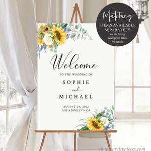 K&ouml;nnte beinhalten: Willkommensschild mit Sonnenblumen, Gr&uuml;npflanzen und wei&szlig;en Blumen. Das Schild lautet "Willkommen zur Hochzeit von Sophie und Michael, 25. August 2022, Los Angeles, Kalifornien".
