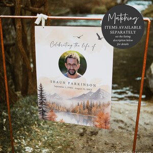 May include: A memorial sign with a watercolor background of a lake and mountains in fall colors. The sign says "Celebrating the life of Shaun Parkinson" with dates of birth and death. A photo of Shaun is in a circle at the top of the sign.