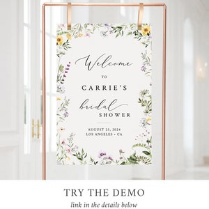 May include: A floral-themed bridal shower welcome sign with a white background and a green, yellow, and purple floral border. The text reads "Welcome to Carrie's Bridal Shower August 25, 2024 Los Angeles, CA".