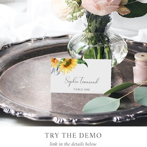 May include: A white place card with a sunflower and floral design. The text on the card reads "Sophie Townsend, Table One".