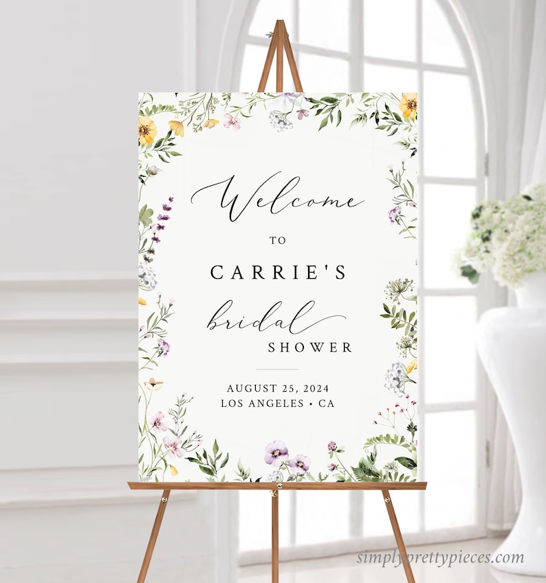 May include: A white bridal shower welcome sign with a floral border. The sign says "Welcome to Carrie's bridal shower, August 25, 2024, Los Angeles, CA".