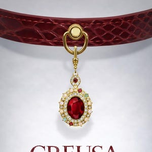 May include: A red leather pet collar with a gold-toned clasp and a pendant. The pendant features a large oval red gemstone surrounded by smaller gems. The word "CREUSA" is displayed below the collar.