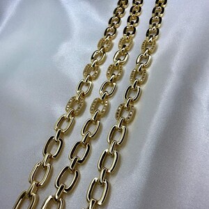 May include: Three gold-colored chain bracelets with a polished finish. Each bracelet features a series of elongated oval links, with some links adorned with small, sparkling embellishments. The bracelets are displayed on a white, satin-like surface.