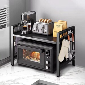 Puede incluir: Estantería de cocina de metal negro con horno, tostadora y cafetera integrados. El horno muestra un temporizador y temperatura digitales. La estantería también contiene utensilios de cocina y guantes de horno.