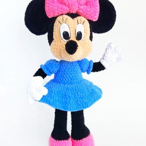 May include: A handmade plush doll of a cartoon mouse character. The doll has black ears, a pink bow, and a blue dress. The doll's feet are pink, and it is wearing white gloves. The doll is approximately 30 cm tall.
