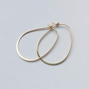 May include: A pair of gold-colored teardrop-shaped hoop earrings. The earrings have a simple, elegant design with a smooth, polished finish. The hoops are lightweight and suitable for everyday wear.