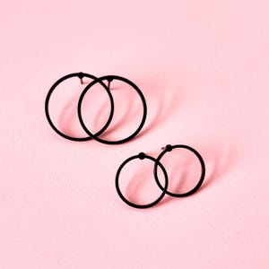 Könnte beinhalten: Zwei Paar schwarze Creolen. Das größere Paar hat zwei Creolen, die miteinander verbunden sind. Das kleinere Paar hat zwei Creolen, die miteinander verbunden sind.