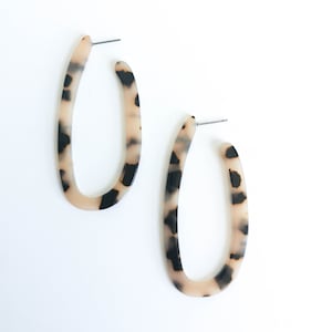 Könnte beinhalten: Ein Paar ovale Ohrringe mit einem Schildpattmuster. Die Ohrringe sind aus cremefarbenem Material mit schwarzen Akzenten.