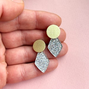 Könnte beinhalten: Ein Paar Ohrringe aus silbernem Glitzer und Gold. Die Ohrringe sind diamantförmig mit einer runden goldenen Scheibe oben.
