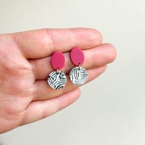 Könnte beinhalten: Ein Paar rosa und weiße Hängeohrringe. Die Oberseite der Ohrringe ist ein durchgehender rosa Kreis. Die Unterseite der Ohrringe ist ein weißer Kreis mit einem schwarzen Zebra-Muster.
