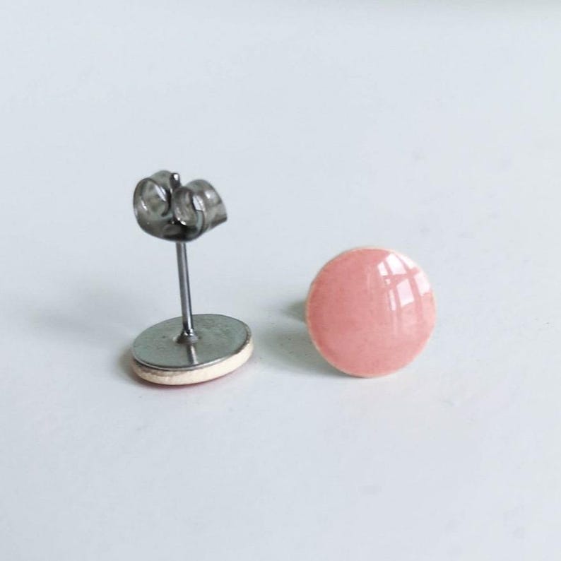 May include: A pair of pink stud earrings. One earring is complete with a post and butterfly backing, the other is a round, glossy pink stud. The earrings are set against a white background.