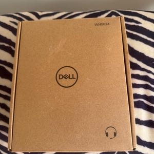 May include: A rectangular brown cardboard box featuring the Dell logo printed in black at the center. The text WH5024 is printed in the top right corner, and a small black icon of a headset with a microphone is located in the bottom right corner.