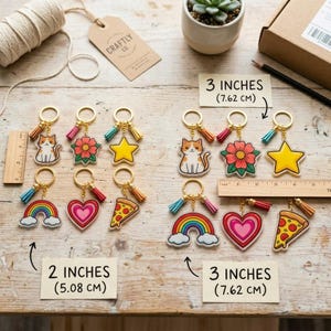 May include: A collection of keychains with various designs, including a cat, flower, star, rainbow, heart, and pizza slice. Each keychain has a gold ring and tassel. The keychains are 2 inches (5.08 cm) and 3 inches (7.62 cm) in size.