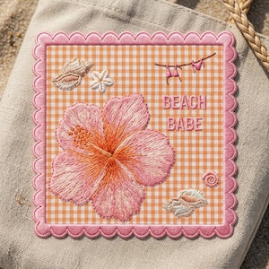 May include: A square fabric patch with a scalloped pink border featuring an orange and white gingham background. The embroidery includes a large pink hibiscus flower, two seashells, a small white flower, and a bikini hanging on a line with the text BEACH BABE.