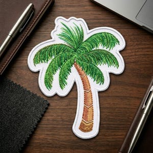May include: An embroidered patch shaped like a palm tree with a brown textured trunk and vibrant green fronds. The design features a thick white border outline, showcasing detailed stitching that creates a realistic texture for the tree leaves.