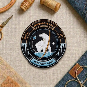 May include: Embroidered patch with a polar bear design, featuring the text "PREFIRE & ICE" and "ROCKET LAB". The patch has a black background with white, blue, and orange accents. The NASA and JPL logos are also visible.