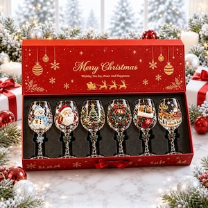 Könnte beinhalten: Ein Set aus sechs klaren Weingläsern in einer roten Geschenkbox mit dem Text Merry Christmas Wishing You Joy, Peace And Happiness. Jedes Glas zeigt ein einzigartiges, handbemaltes Weihnachtsmotiv, darunter ein Schneemann, der Weihnachtsmann, ein Baum, ein Kranz, ein Strumpf und ein Rentier.