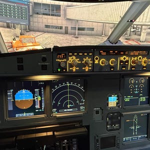 May include: An aircraft cockpit interior with multiple illuminated display screens and control panels. The screens display flight data and navigation information. The cockpit is dark grey with yellow and orange lighting. An orange vehicle is visible through the windscreen.