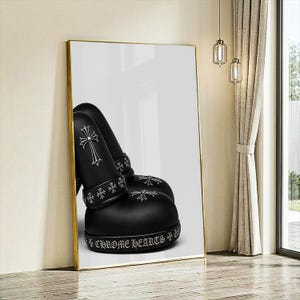 May include: A framed wall art print featuring a pair of matte black boots with silver-toned cross emblems. The boots are adorned with a band of small cross motifs and the text CHROME HEARTS printed in a gothic font along the thick rubber sole.