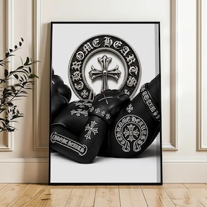 May include: A framed wall art print featuring a black figure adorned with silver Chrome Hearts branding and cross motifs. The design includes a prominent circular emblem with the text Chrome Hearts and a central cross, set against a white background.