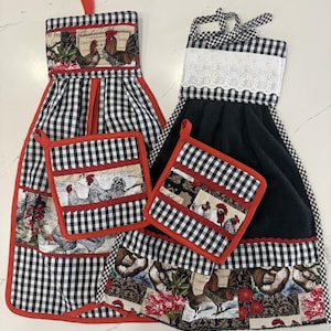 May include: Two hanging kitchen towels and two matching pot holders. One towel features a black and white gingham pattern with a rooster print and red trim. The other towel has a black fabric section, white lace trim, and a rooster print border.